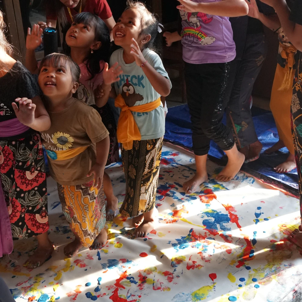 Children from House of Hope in Bali laughing and looking up from a paint-covered canvas